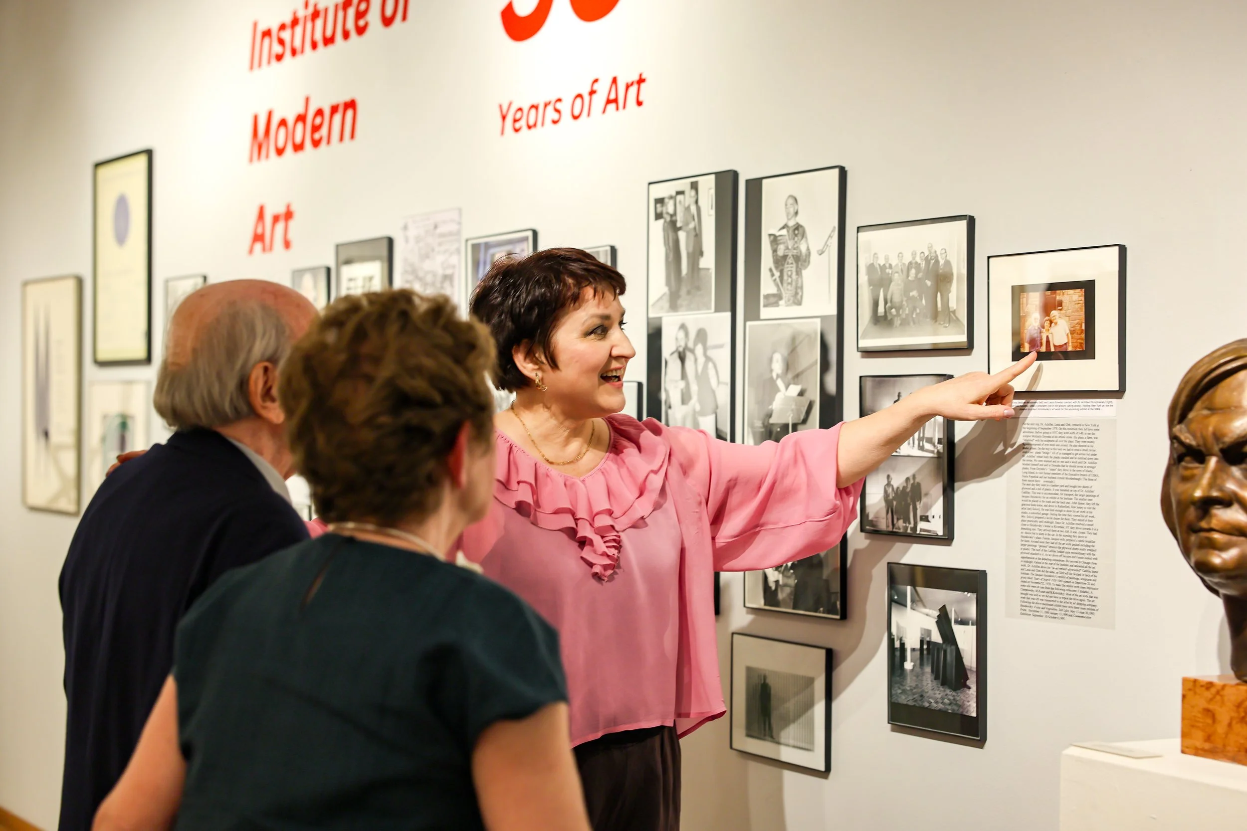 UIMA president Motria Melnyk pointing out photographs on a wall retrospective celebrating fifty-five years of the Institute