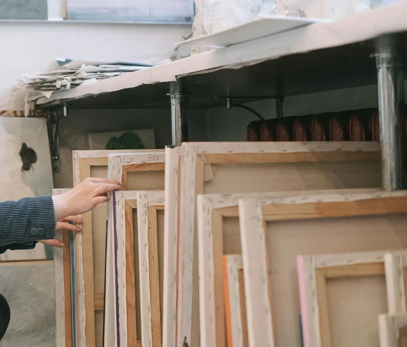 A hand sorting stretched canvases and works on paper in a studio storage space